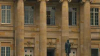 Vista elegante de un edificio clásico con pilares y una estatua en la entrada.