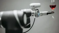 Un brazo robótico sosteniendo cuidadosamente una copa de vino tinto contra un fondo neutral, mostrando la innovación.