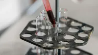Red liquid being transferred into test tubes in a lab setting for research.