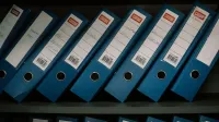 Carpetas de oficina azules ordenadamente ordenadas con fechas y nombres para almacenamiento organizado.