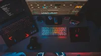 Un espacio de trabajo contemporáneo con monitores duales, un teclado iluminado con arcoíris y software de edición, perfecto para los entusiastas de la tecnología.