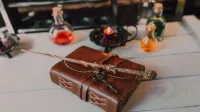 Un libro de hechizos vintage con una varita mágica y botellas de poción en una mesa rústica, evocando vibraciones místicas.