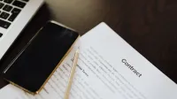 Close-up de un documento de contrato junto con un smartphone y una laptop, ideal para conceptos de negocio.