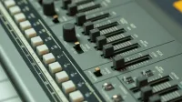 Vista detallada de una consola de mezcla de música con varios controles deslizantes y botones en una configuración de estudio.