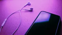 Una imagen de primer plano de un teléfono inteligente y auriculares contra un fondo púrpura, destacando la tecnología moderna.
