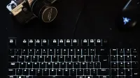 Una configuración tecnológica con poca luz que incluye un teclado iluminado, una cámara vintage y un mouse moderno.