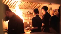 Chefs profesionales que trabajan en una cocina industrial ocupada con llamas visibles.