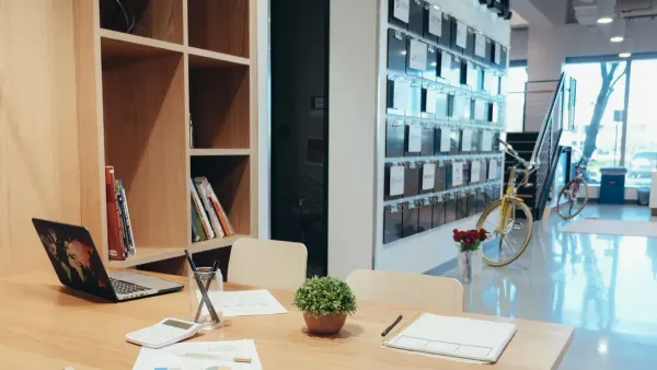 A modern office workspace featuring a laptop, documents, and a potted plant on a wooden table.