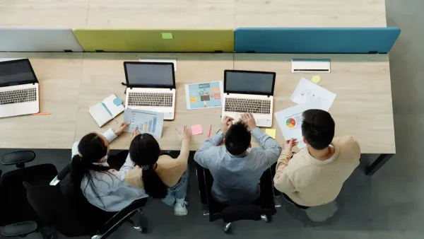 Aerial view of four colleagues working with laptops and documents at a shared desk.