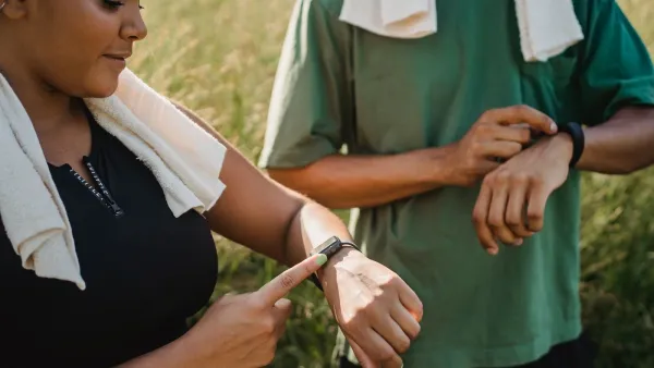 Two people checking their fitness watches while taking a break from a workout outside.