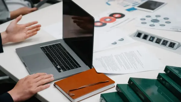 Primer plano de una mesa de reuniones de negocios con una computadora portátil, documentos y discusión en curso.