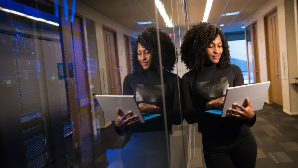 Mujer afroamericana de pie en la oficina moderna usando una computadora portátil, reflejando el profesionalismo y el compromiso de la tecnología.