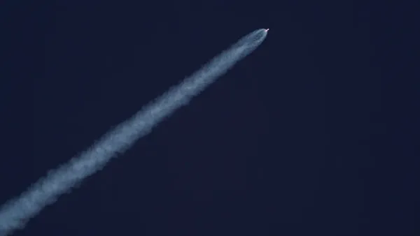 Un cohete asciende hacia el cielo, dejando un rastro de humo contra el cielo azul claro.