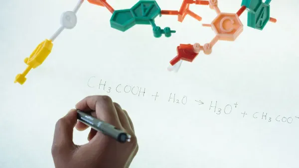Escritura anónima de químico con marcador en tablero magnético iluminado Fórmula de producción de hidronio y acetato después de estudiar el modelo plástico de molécula en laboratorio