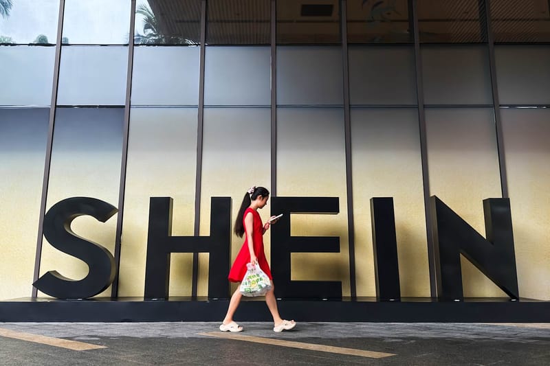 Una mujer mira su teléfono inteligente mientras camina junto a un anuncio de Shein