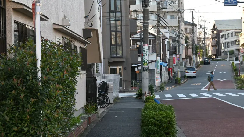 A peaceful urban street in Japan with a lone pedestrian crossing and residential buildings.