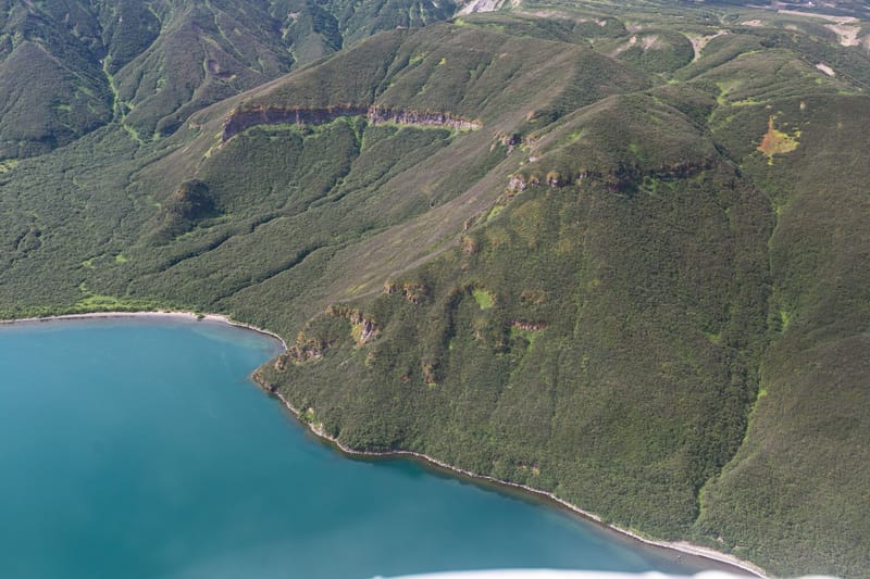 A stunning aerial view of a green mountain range beside a serene coastline.