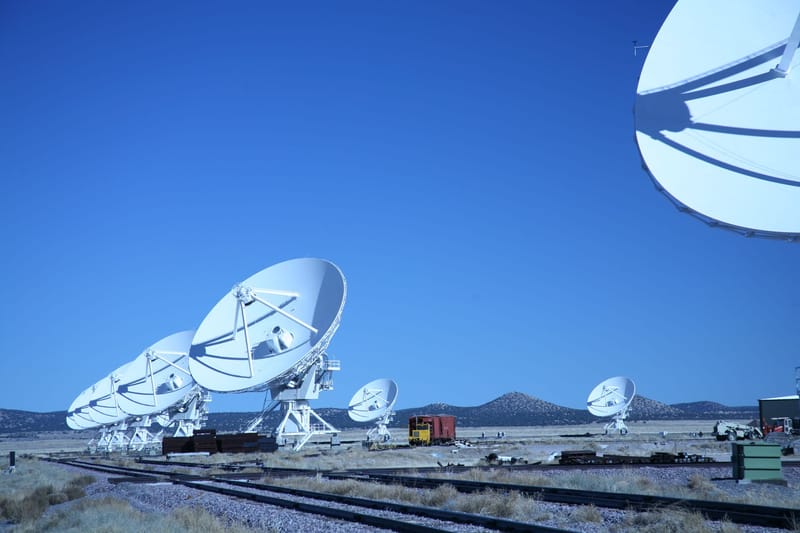 Multiple satellite dishes aligned in a field against a vibrant blue sky, showcasing modern communication technology.