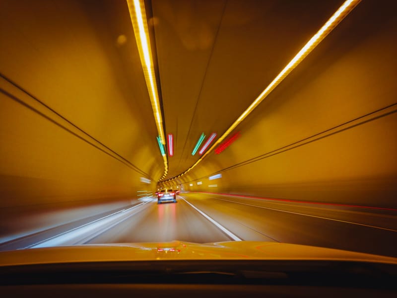 Blurry traffic scene with cars speeding through a brightly lit tunnel at night.