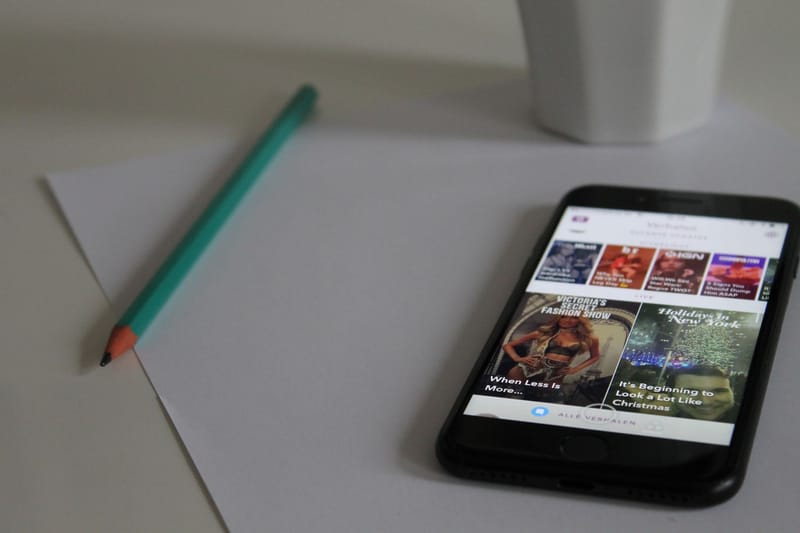 Smartphone displaying news, next to pencil and paper on a desk, showcasing modern technology in a workspace.