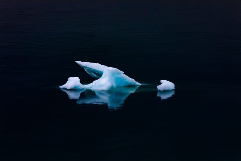 A serene scene of a floating iceberg with reflection on calm ocean waters during winter.