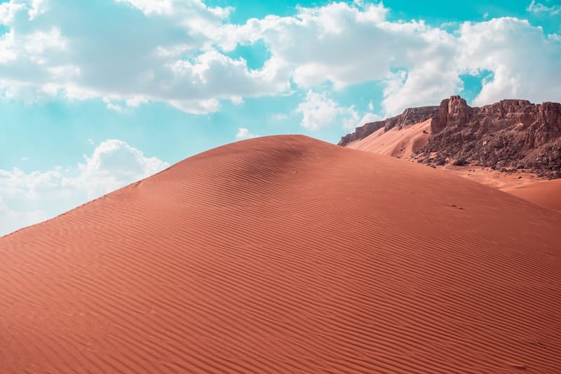 Stunning red sand dunes under a bright blue sky with clouds, creating a dramatic desert landscape.