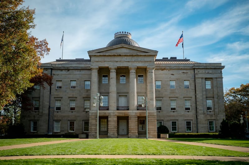 Front view of the historic North Carolina State Capitol in Raleigh, showcasing neoclassical architecture under a blue sky.