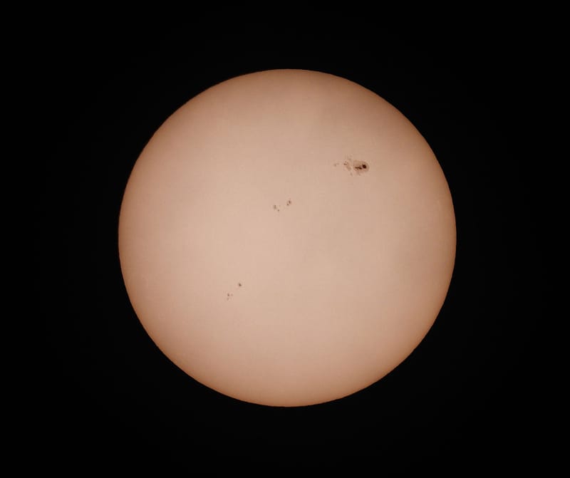 A detailed photograph of the sun highlighting visible sunspots against a dark background.
