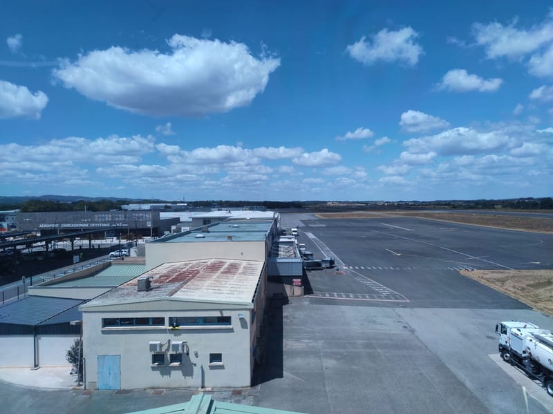 Aerial view of a sunny airport with runway and terminal buildings under blue sky.