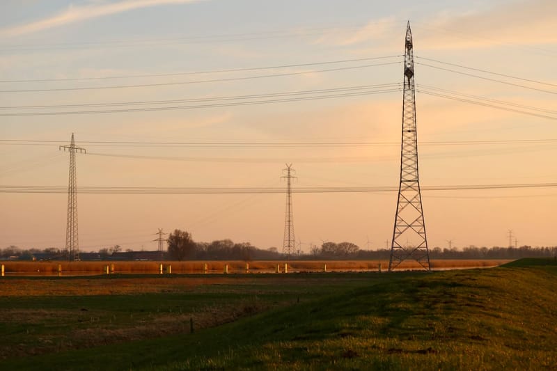 Power lines stretch across a rural landscape at sunset, creating a serene and industrial scene.