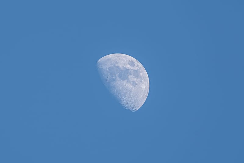 A high-resolution image of the moon during its waxing gibbous phase against a clear blue sky.