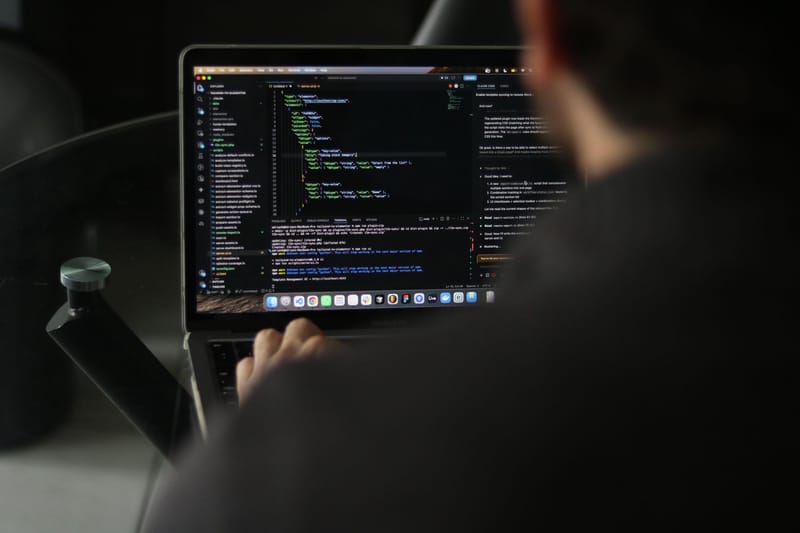 A focused developer writing code on a laptop in an indoor workspace.