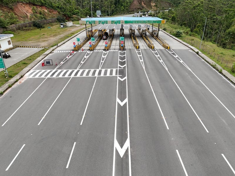Aerial shot of an empty multi-lane toll booth on a highway surrounded by greenery.