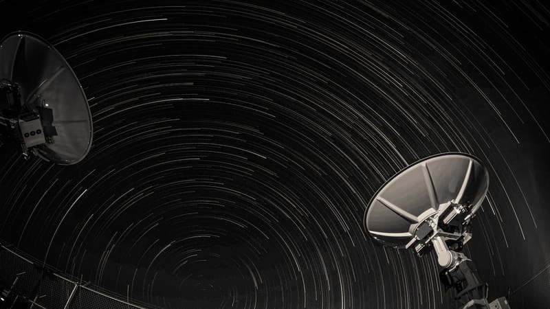 Long exposure of star trails creating circular patterns over two satellite dishes against a night sky.