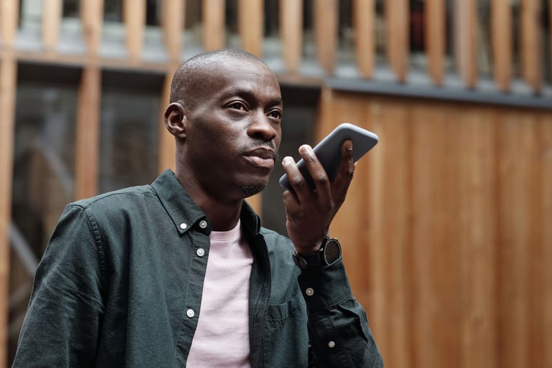 Stylish adult man using his smartphone for voice commands in an outdoor urban setting.