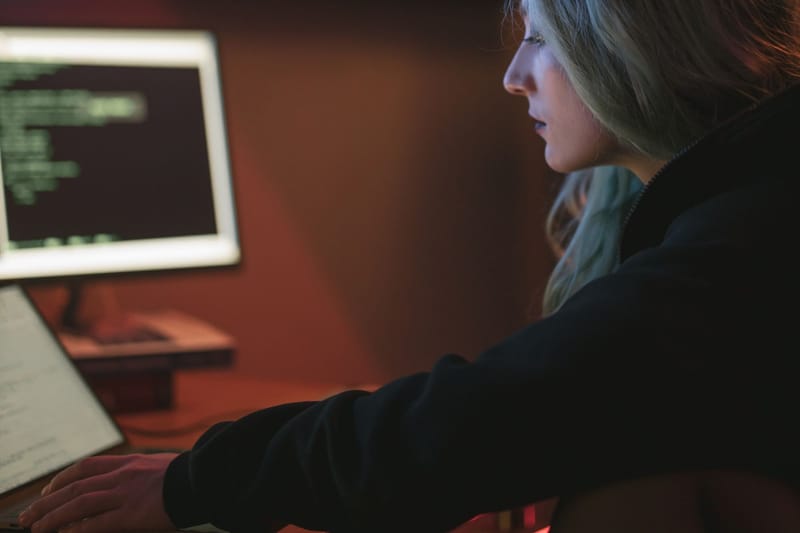 A woman working late on a laptop with code displayed on the screen in a dark room.