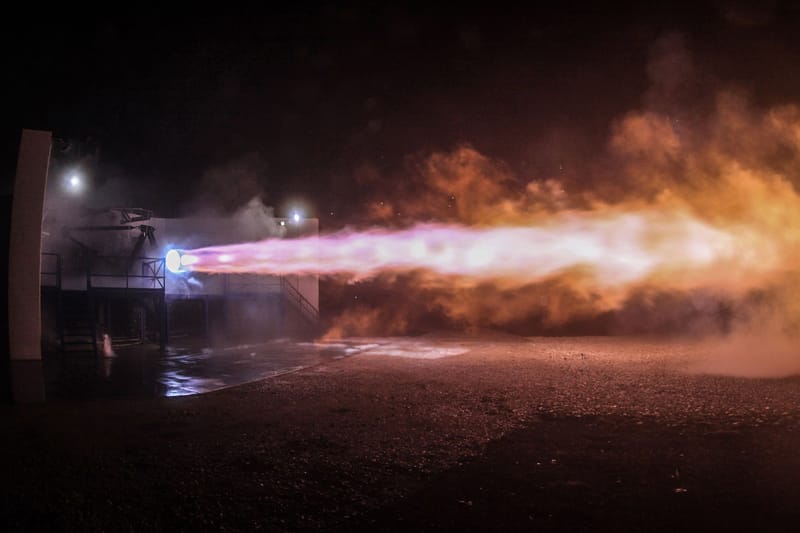 A powerful rocket engine test firing with vibrant flames illuminating the night sky.