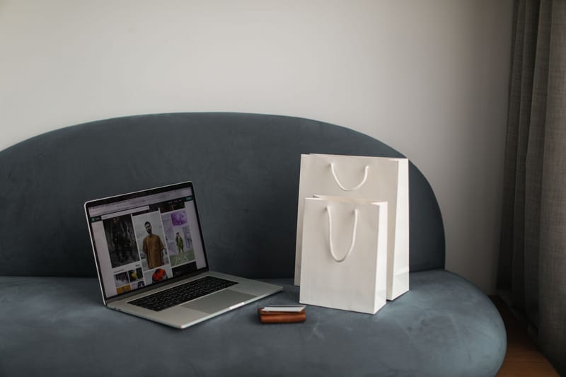 Online shopping setup with a laptop and shopping bags on a stylish couch.