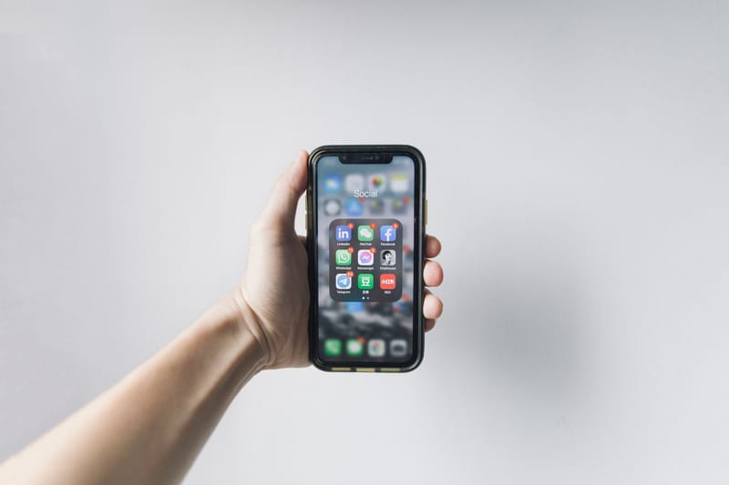 Hand holding smartphone displaying social media apps on home screen.