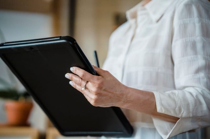 Close-up of a woman holding a digital tablet in an office environment, focusing on hand details.