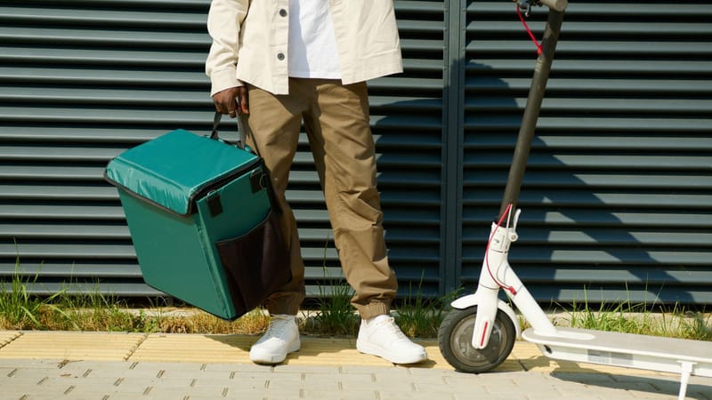 Delivery person with an insulated bag and electric scooter on the street.