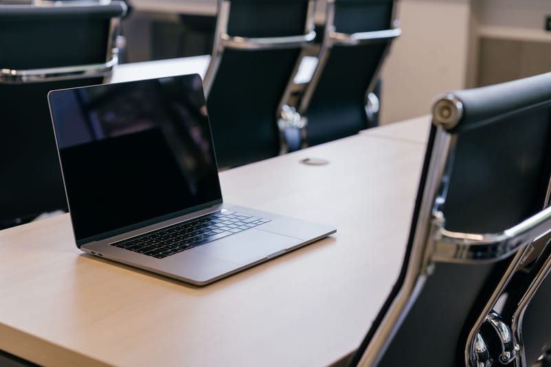 Open laptop on a wooden conference table with stylish black chairs in a modern office setting.