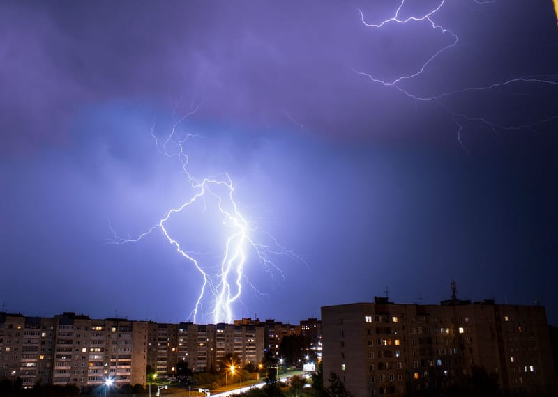 Striking lightning bolt illuminates cityscape during a nighttime thunderstorm.