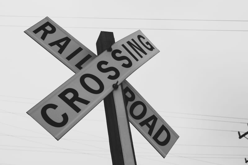 Black and white photo of a railroad crossing sign against a clear sky.