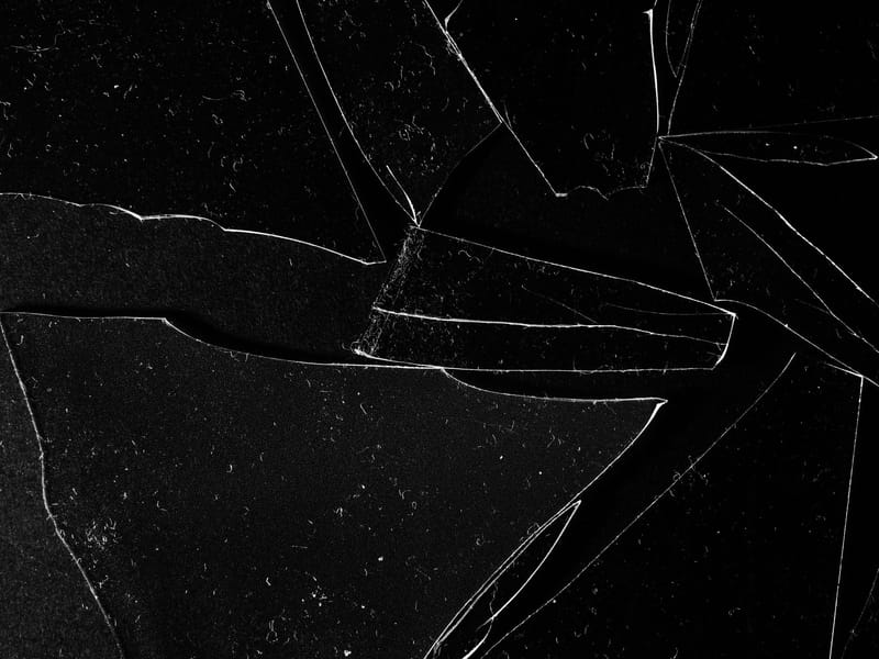 Close-up of cracked glass pieces on a black surface, emphasizing sharp edges.