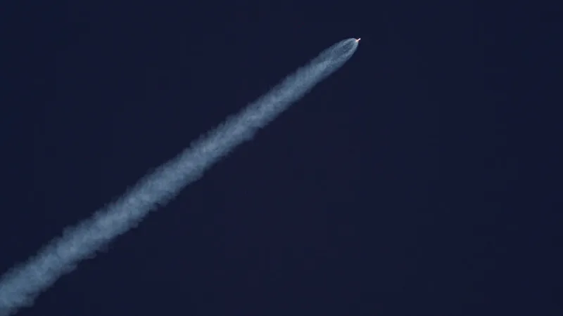 A rocket ascends into the sky, leaving a trail of smoke against the clear blue sky.