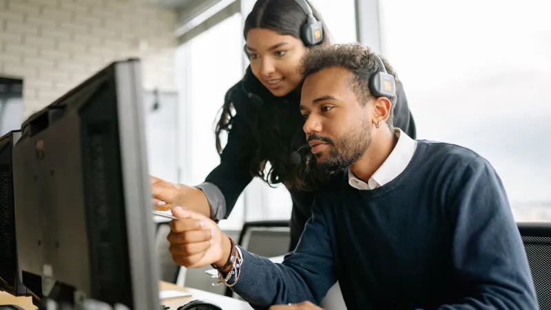 Two call center employees working together with headsets in a modern office setting.