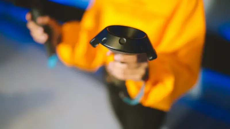 A person in a bright yellow sweater holds virtual reality controllers indoors.