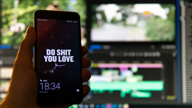 Close-up of a smartphone displaying an inspirational message against a video editing background.