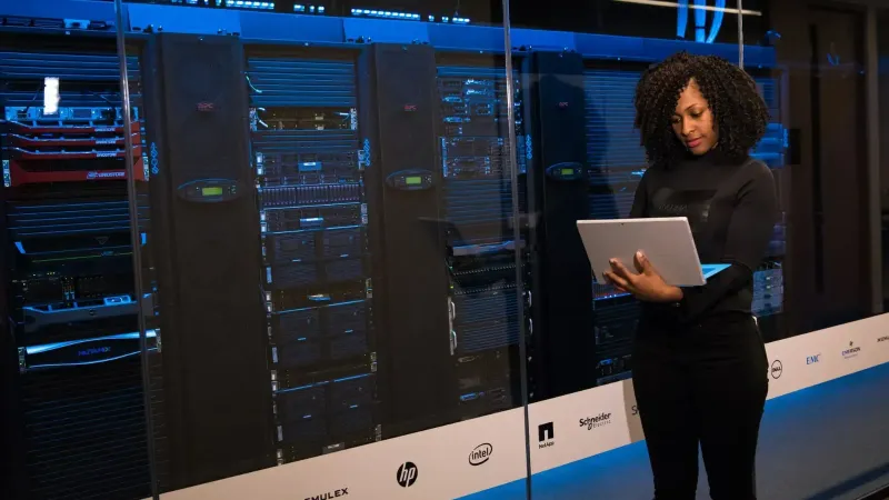 Una ingeniera que usa una computadora portátil mientras monitorea los servidores de datos en una moderna sala de servidores.